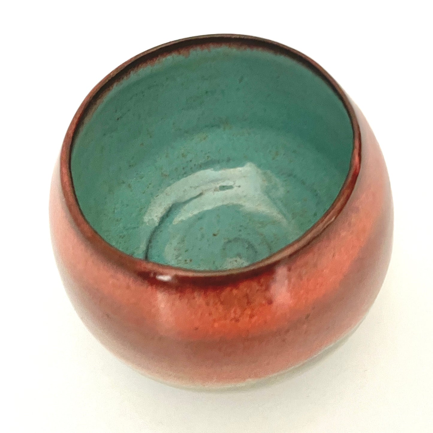 Round red cup with Turquoise interior on Dark Clay